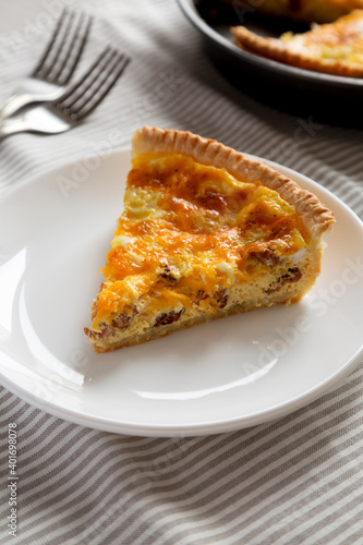 Homemade Bacon Quiche with Eggs and Cheddar Cheese on a white plate, low angle view.