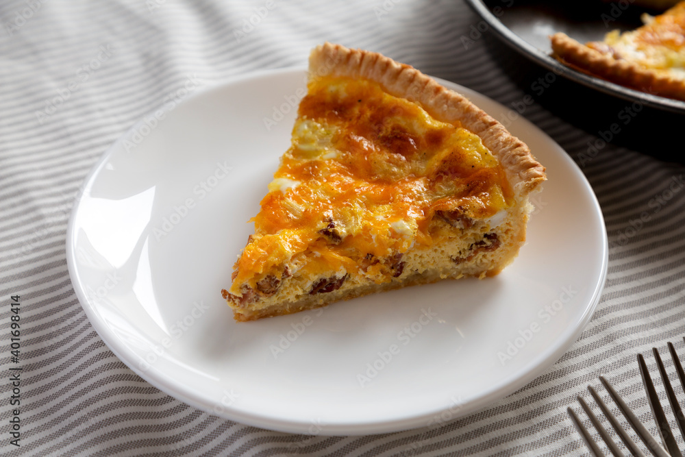 Homemade Bacon Quiche with Eggs and Cheddar Cheese on a white plate, low angle view. Close-up.