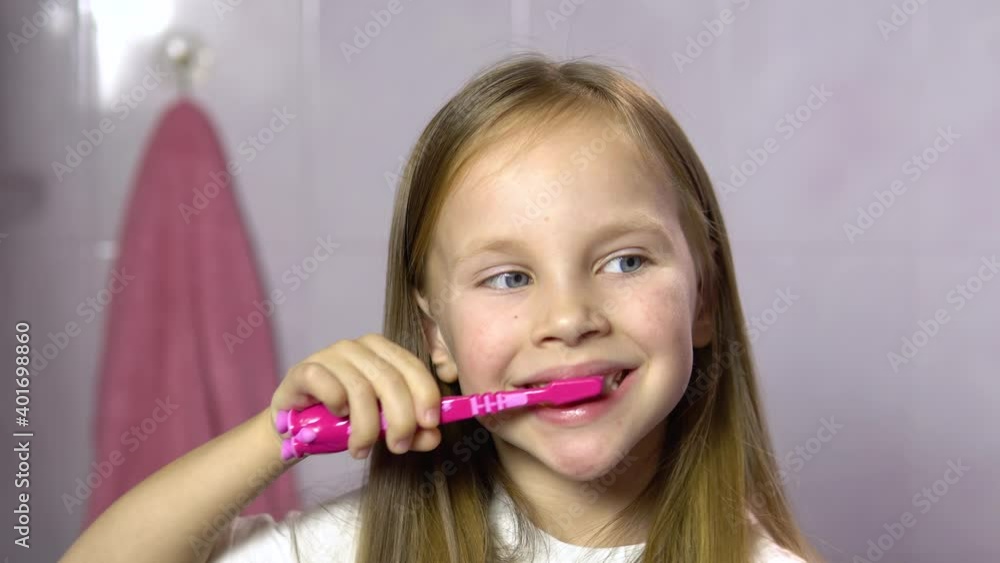 Little blonde girl brushes her teeth in the bathroom.Close-up.A 4-5 year old girl is brushing her teeth with a pink toothbrush. Little blonde girl brushes her teeth in the bathroom.Close-up.A 4-5 year old girl is brushing her teeth with a pink toothbrush.