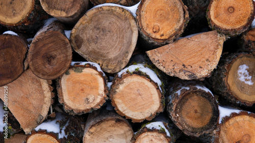 Panorama of stacked wooden sawn logs covered with snow and laid out in several rows. Wooden natural background. Close up view of dry firewood.