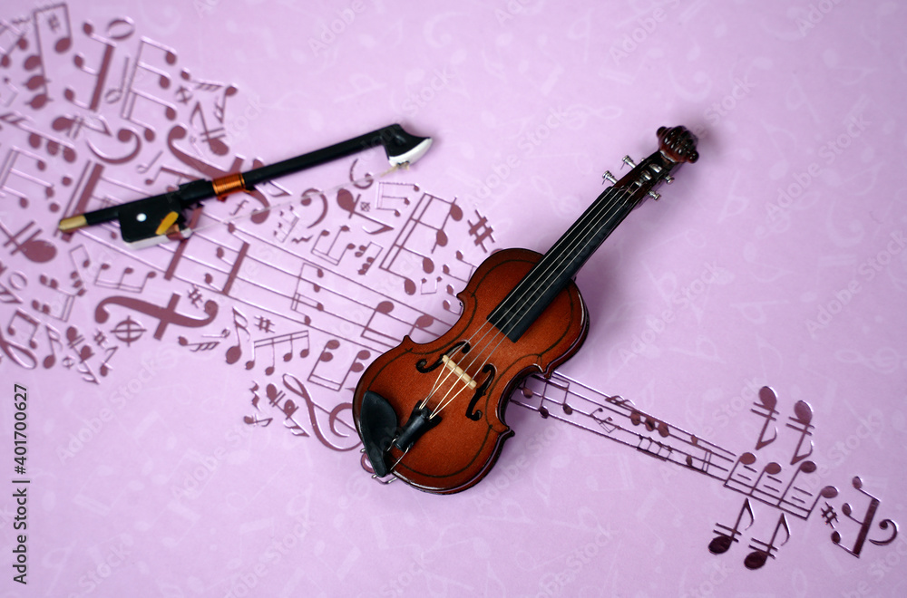 Fototapeta premium Miniature violin on a pink background with notes