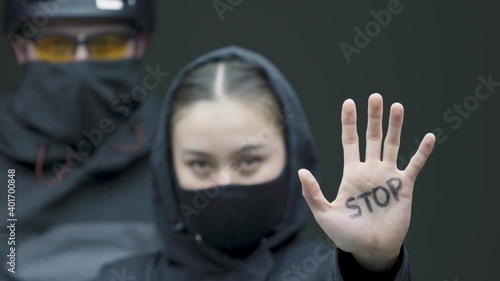 Protesting female demonstrator show stop gesture by hand. Woman with activist in black masks on picket