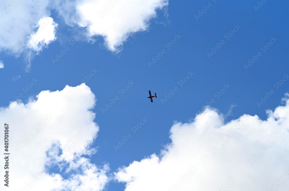 A small silhouette of an airplane in a blue sky with clouds