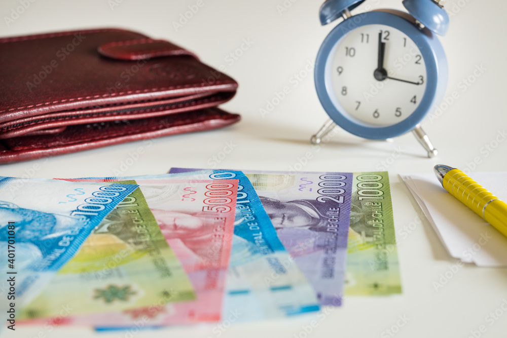 Chile currency, pesos, next to the wallet and the clock showing five to twelve Chile currency, pesos, next to the wallet and the clock showing five to twelve