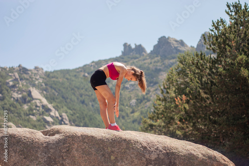 Portrait of a runner girl in summer sports clothes exercising on top of a rock on a mountain on a sunny day