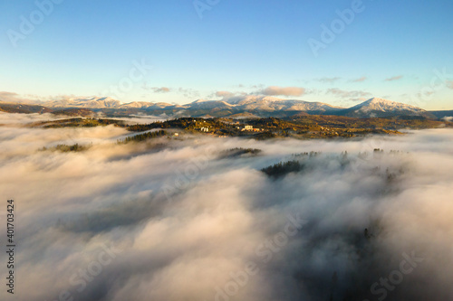 Aerial view of a small distant village houses on hill top in fall foggy mountains at sunrise.