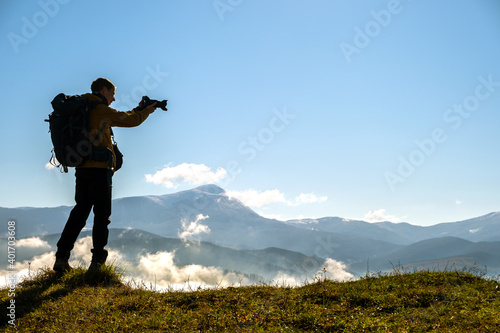 Silhouette of a backpacker photographer taking pictures of morning landscape in autumn mountains with digital camera. © bilanol