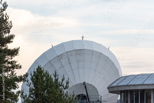 Big satellite dish antennas hidden in green pine tree forest communication center on bright blue white background