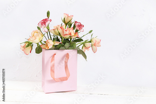 Roses with a gift on a pink table, abstract spring floral background. Creative modern bouquet, minimal holiday concept. Greeting card for Women's Day or Mother's Day, happy birthday, wedding