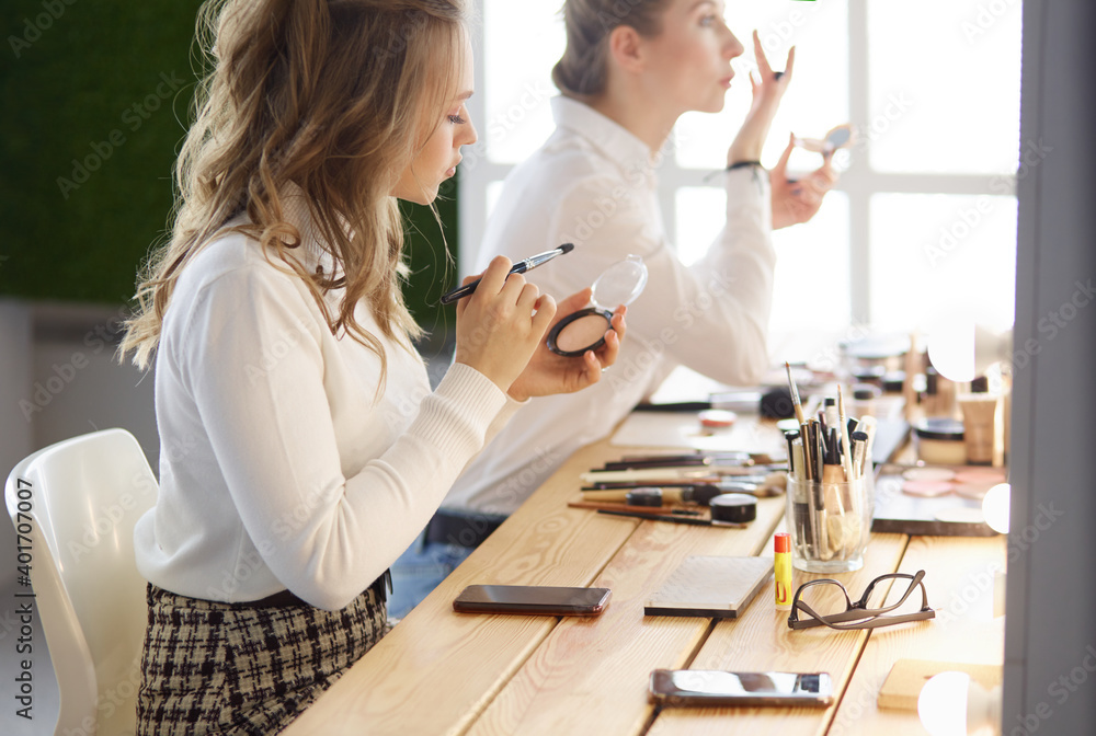 Naklejka premium Make-up artist applying white eyeshadow in the corner of model's eye and holding a shell with eyeshadow on background