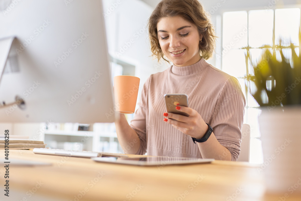 Young businesswoman text messaging while sitting at office in front of laptop Young businesswoman text messaging while sitting at office in front of laptop