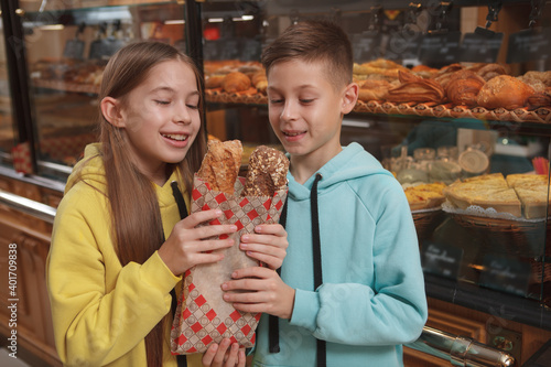 Beautiful young girl and her twin brother holding freshly baked bread at bakery store