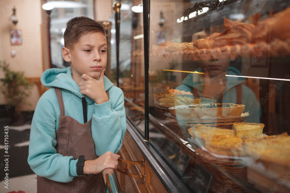 Cute young boy working at his parents bakery cafe, examining retail display