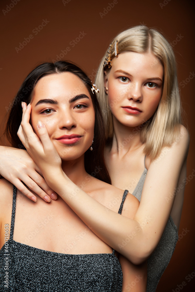two pretty diverse girls happy posing together: blond and brunette on brown background, lifestyle people concept two pretty diverse girls happy posing together: blond and brunette on brown background, lifestyle people concept