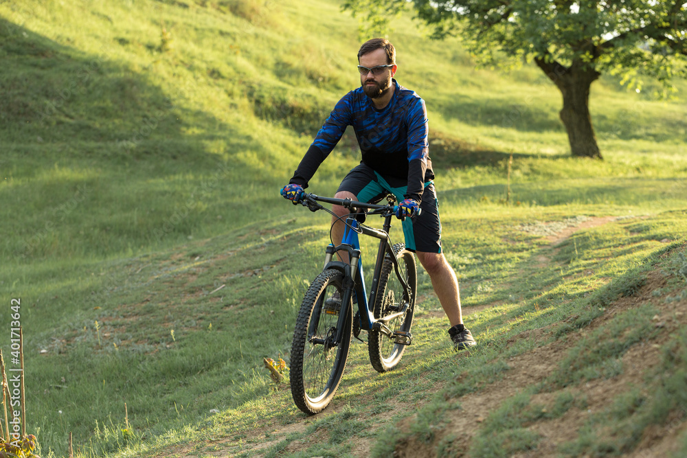 Cyclist in shorts and jersey on a modern carbon hardtail bike with an air suspension fork standing on a cliff against the background of fresh green spring forest Cyclist in shorts and jersey on a modern carbon hardtail bike with an air suspension fork standing on a cliff against the background of fresh green spring forest