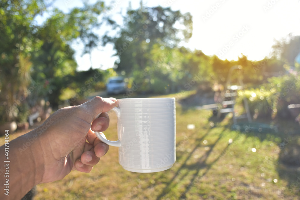 Obraz premium Hand of people holding to white coffee cup for drink. Beautiful and fresh time of people holding coffee cup for drink isolated on garden background with soft sunlight.