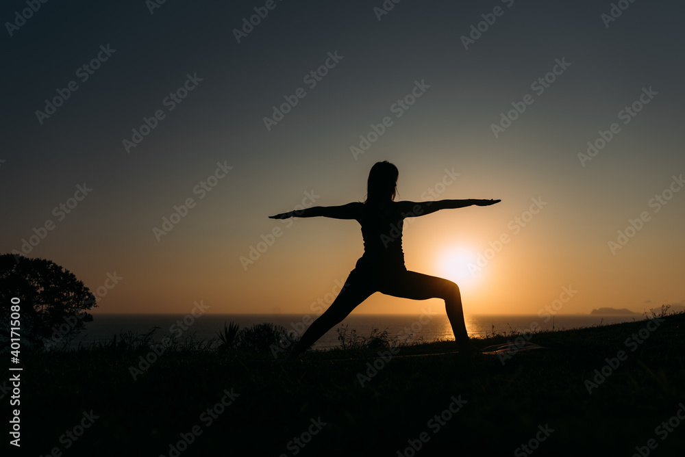 Woman doing yoga on the coast and with a beautiful sunset in the background