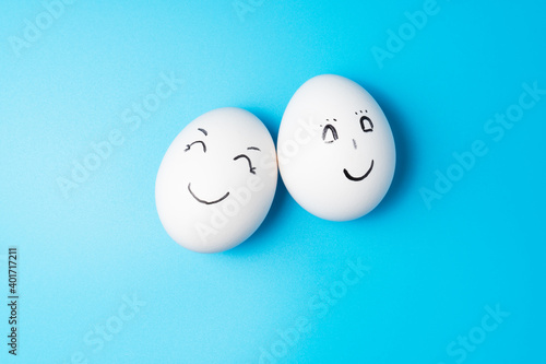 Two white chicken eggs with smiling faces on blue background.