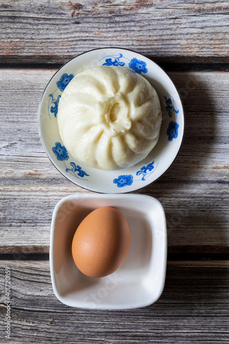 Photography Flat lay of a steamed stuffed bun in a small ceramic plate and a boiled egg on small bowl on rustic wooden table