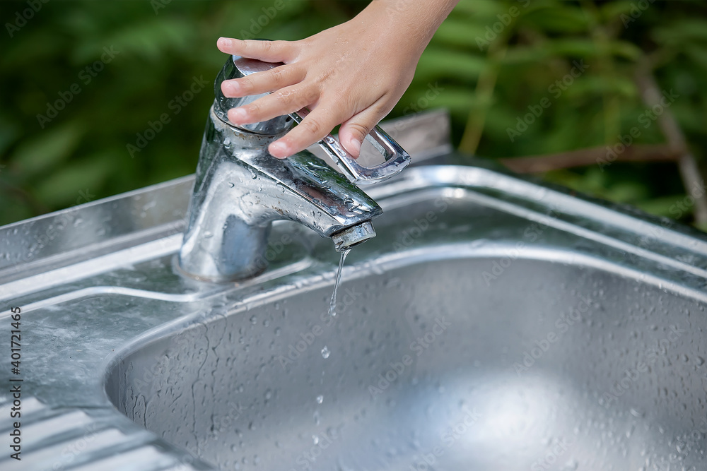 Baby try to turn off water faucet but water still leak. A child's hand
