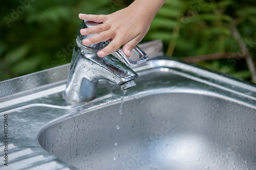 Baby try to turn off water faucet but water still leak. A child's hand turning off the tap. Save water. World Water Monitoring Day. Environment and health care concept. Natural green background