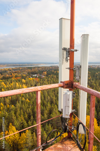 Cellular microwave system. 3G, 4G sector antennas and transceiver unit based on telecommunication tower metal construction. Autumn pine tree forest and blue epic sky background. photo