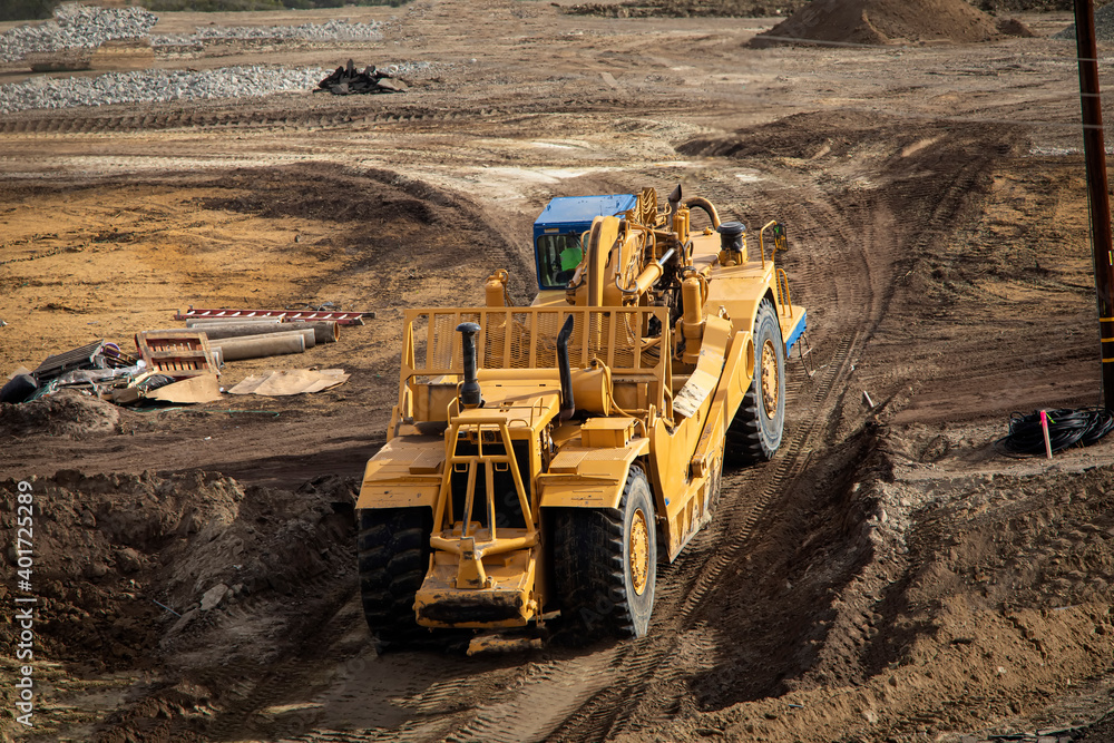 Heavy earthmoving equipment including scapers and motor graders involved in grading operations at a construction site - obrazy, fototapety, plakaty 