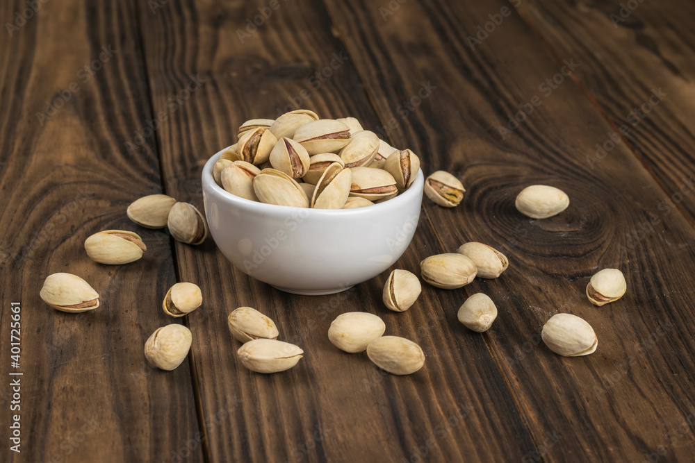 A white bowl on a wooden table with fried pistachios. A white bowl on a wooden table with fried pistachios.