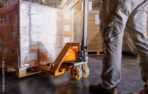 Warehouse worker working with hand pallet jack unloading cargo boxes at the warehouse storage. shipment boxes.