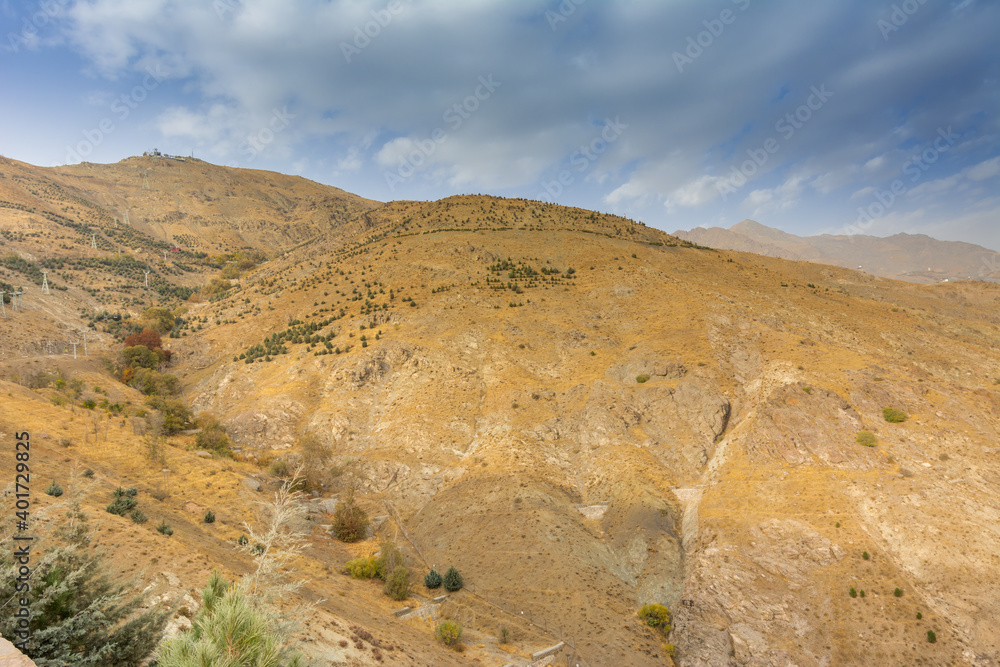 Tochal mountain ridge with rocks and trees in autumn against blue sky, Tehran, Iran. Tochal is a popular recreational region for Tehran's residents