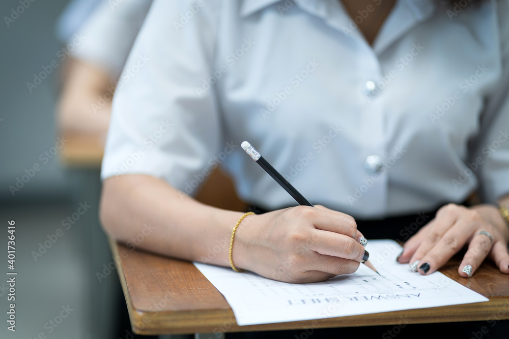 Close up of young university students concentrate on doing examination in classroom. Girl student writes on the examinations answer paper in the classroom. Close up of young university students concentrate on doing examination in classroom. Girl student writes on the examinations answer paper in the classroom.