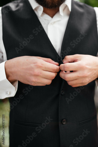 The groom buttons his jacket