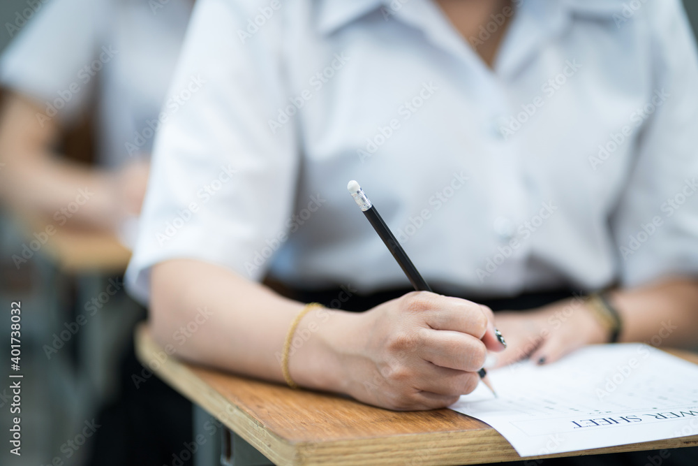 Close up of young university students concentrate on doing examination in classroom. Girl student writes on the examinations answer paper in the classroom. Close up of young university students concentrate on doing examination in classroom. Girl student writes on the examinations answer paper in the classroom.