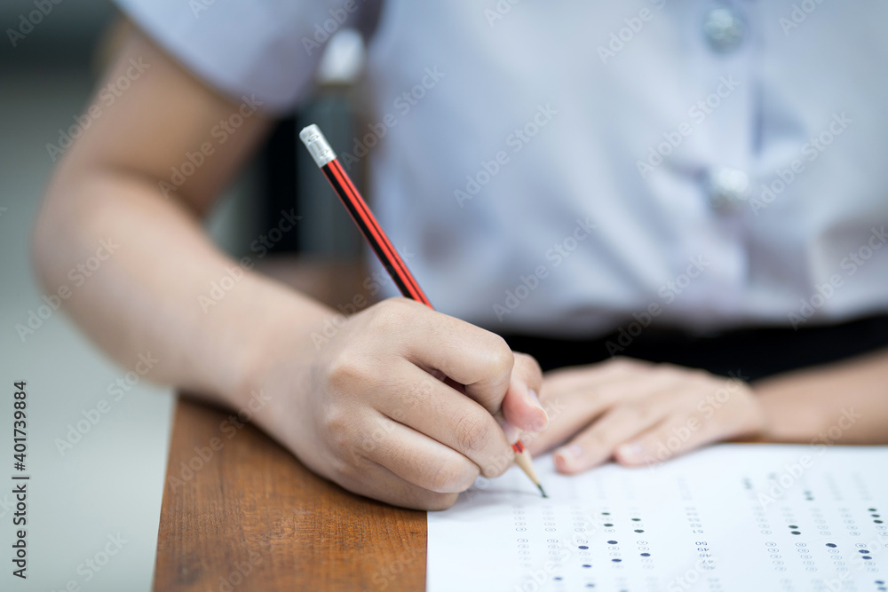 Close up of young university students concentrate on doing examination in classroom. Girl student writes on the examinations answer paper in the classroom. Close up of young university students concentrate on doing examination in classroom. Girl student writes on the examinations answer paper in the classroom.