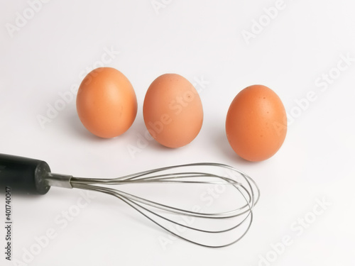 Egg beater with chicken eggs in a bowl isolated on white background.