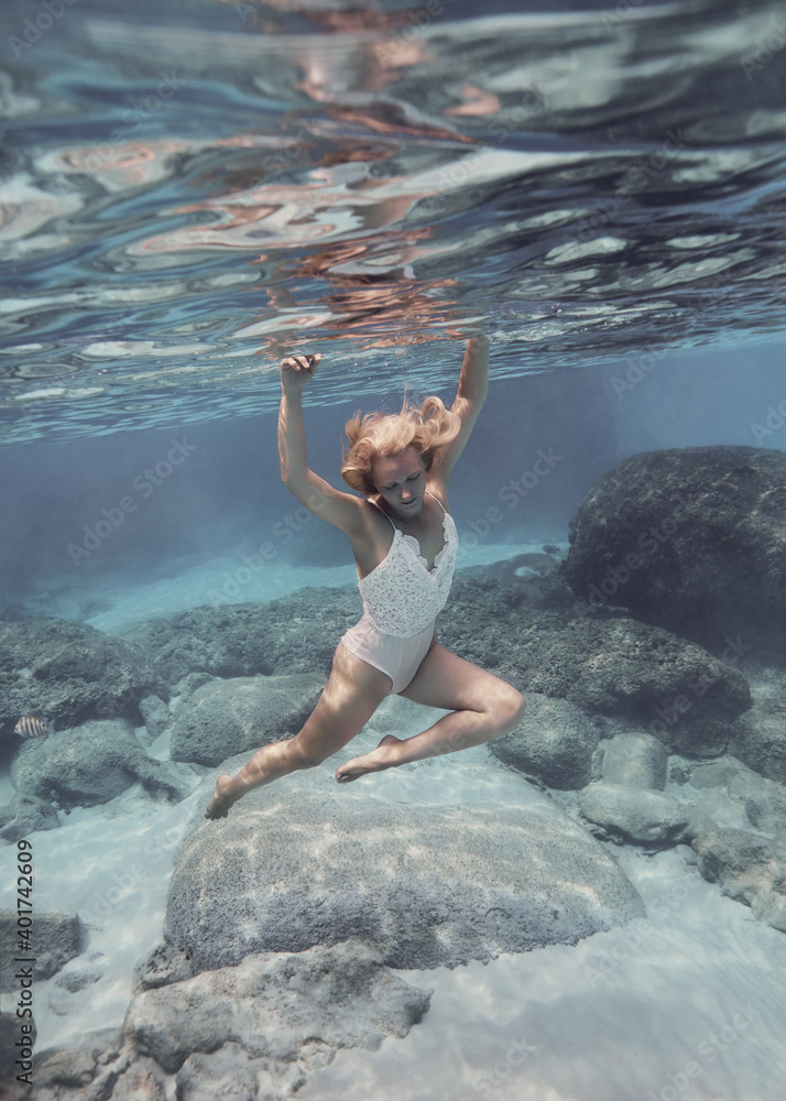 Fototapeta premium Woman in white swimsuit swims underwater in the crystal clear water of the tropical sea