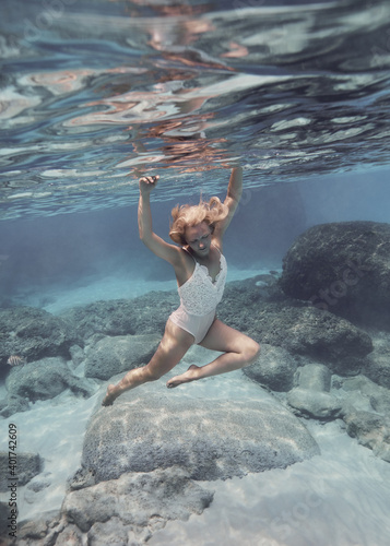 Woman in white swimsuit swims underwater in the crystal clear water of the tropical sea