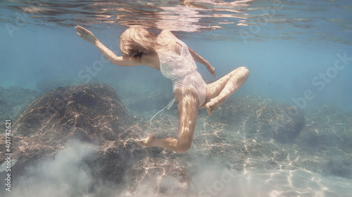 Woman in white swimsuit swims underwater in the crystal clear water of the tropical sea