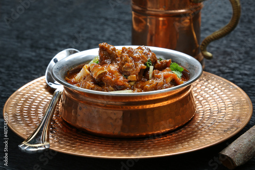 Pakistani famous North Indian curry lamb gosht mutton nirahi karahi kadai bronze bowl black background garnished with chilly  photo