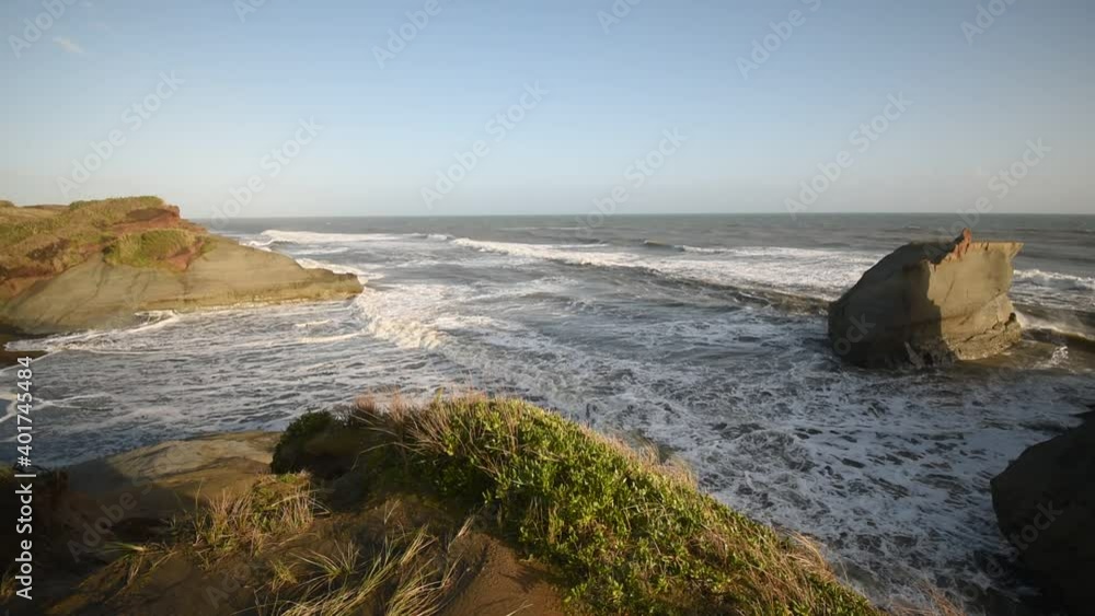 Surf rolling in against the cliffs, rock stacks and black sand at Waverley Beach, South Taranaki, New Zealand. Taken in the warm late afternoon light. Surf rolling in against the cliffs, rock stacks and black sand at Waverley Beach, South Taranaki, New Zealand. Taken in the warm late afternoon light.
