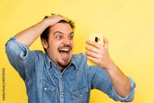 A young Caucasian male showing excitement after seeing something on the phone against a yellow background photo