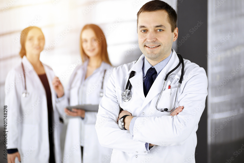Professional middle aged doctor with a stethoscope and crossed arms at work, standing together with his female colleagues in a sunny clinic. Perfect medical service in a hospital. Medicine and Professional middle aged doctor with a stethoscope and crossed arms at work, standing together with his female colleagues in a sunny clinic. Perfect medical service in a hospital. Medicine and