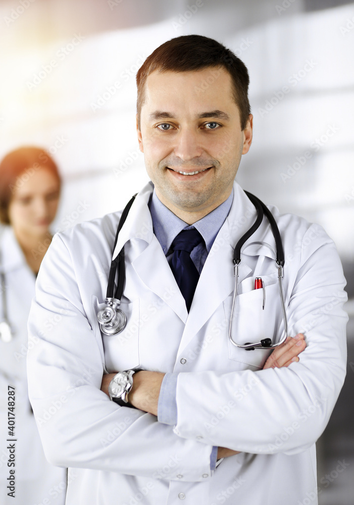 Professional middle aged doctor with a stethoscope and crossed arms at work, standing together with his female colleagues in a sunny clinic. Perfect medical service in a hospital. Modern medicine Professional middle aged doctor with a stethoscope and crossed arms at work, standing together with his female colleagues in a sunny clinic. Perfect medical service in a hospital. Modern medicine