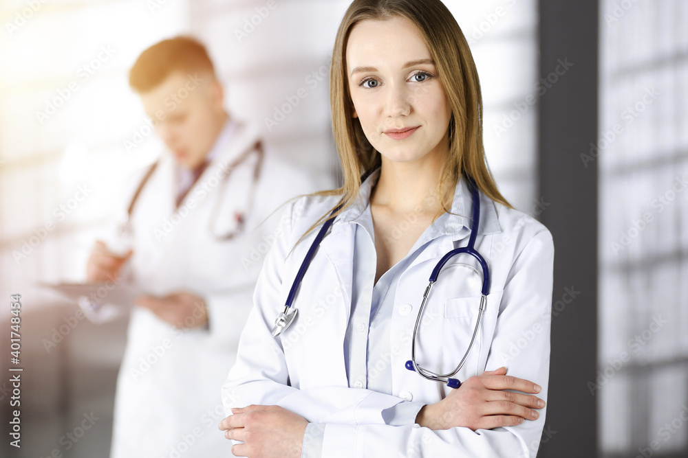 Professional beautiful woman-doctor with a stethoscope is standing straight with crossed arms in a sunny clinic. Young doctors at work in a hospital. Best medicine and healthcare concept