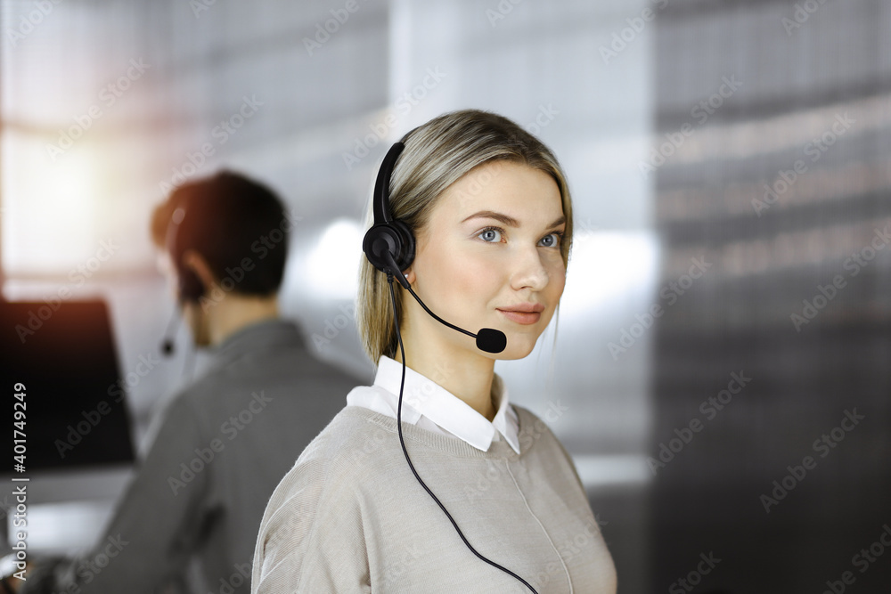Diverse people group in sunny call center. Blonde business woman talking by headset while sitting in modern office Diverse people group in sunny call center. Blonde business woman talking by headset while sitting in modern office