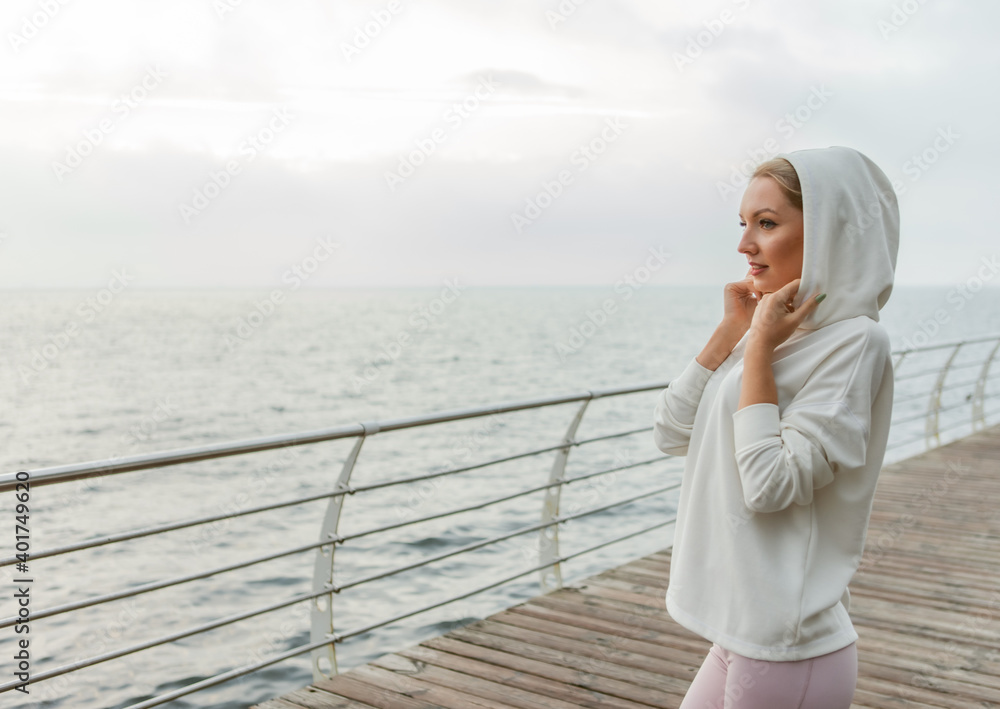 Portrait of attractive cute sportswoman in white hoodie on the beach