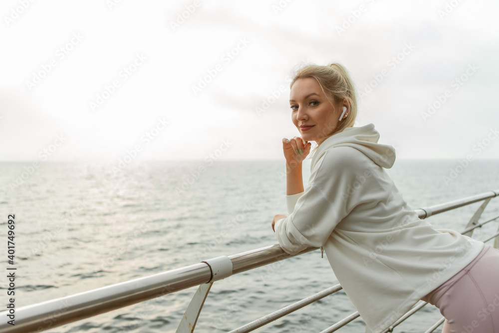 Portrait of a cheerful blonde sportswoman on the beach. Young slim fit woman listening to music with earphones