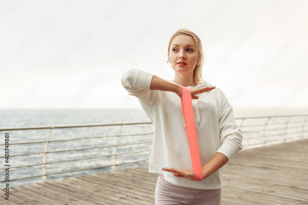 Young fit woman exercises hands with fitness rubber bands on the beach. Healthy lifestyle