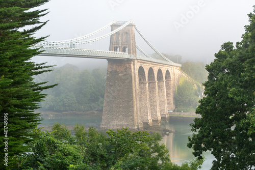 Foggy Menai Suspension bridge in the early morning as the fog lifts with Anglesey in the distance.