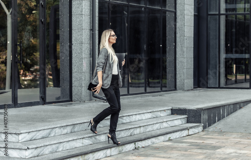 Business woman leaves the office building with a folder in her hands. Office worker. Young lady in business suit